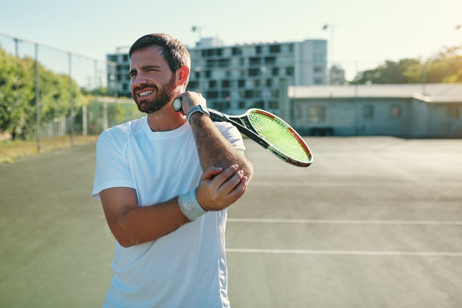 Man holding a tennis racket on the court holding his elbow in pain, potentially due to tennis elbow