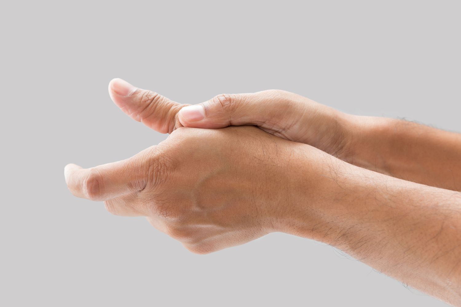 Close up of someone's hands against a grey background. They are rubbing their thumb joint, may be needing a thumb splint